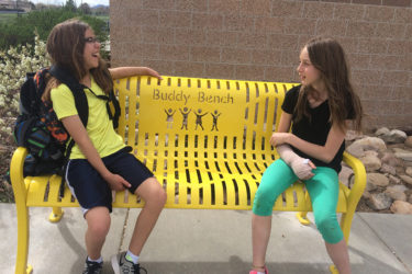 Two girls sit on a Buddy Bench