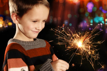 Young boy holding burning sparkler on festive lights background