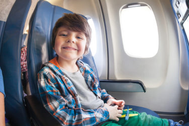 Close shoot of happy little boy sit by the window in commercial jet pane going to vacation