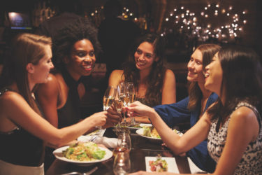 group of female friends dining at a restaurant, clinking together their glasses