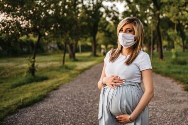 Pregnant woman outdoors wearing a mask