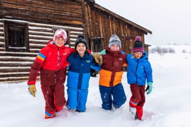 Four kids in snow wearing Town Hall winter clothing.