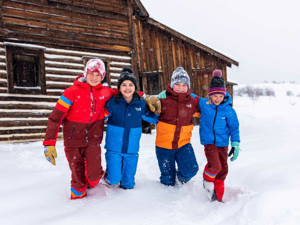 Four kids in snow wearing Town Hall winter clothing.