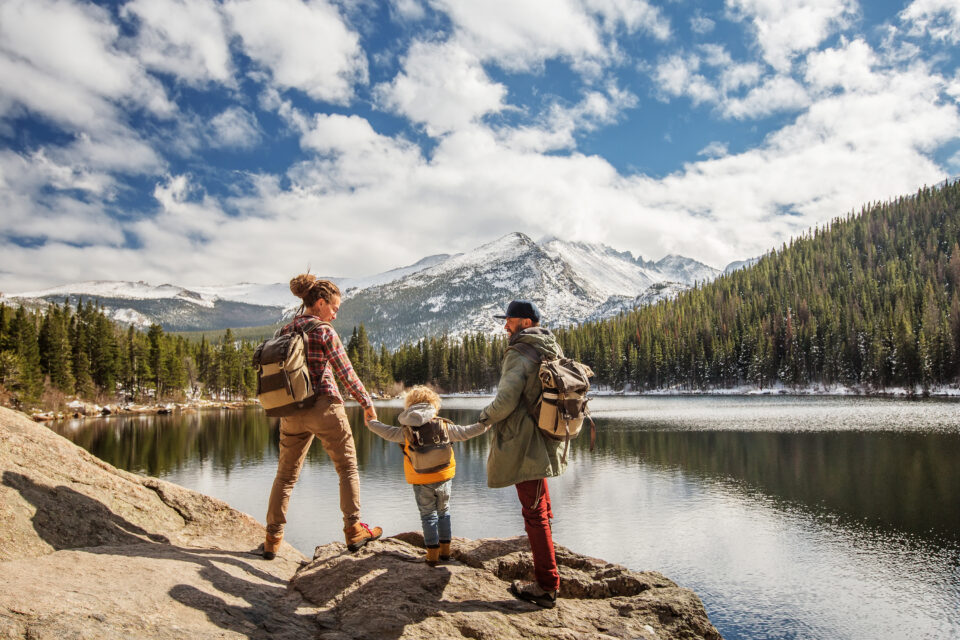 family walking on rocks next to a large lake with trees and mountains
